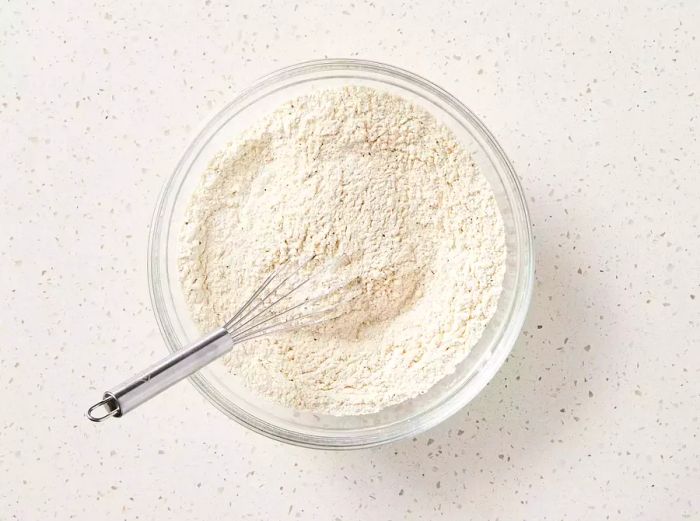 A large bowl filled with flour, garlic salt, pepper, paprika, and poultry seasoning, all being whisked together.