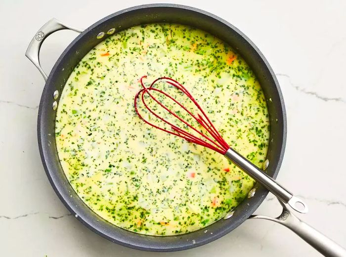 A bird’s-eye view of chicken broth and half-and-half being stirred into the cooked vegetables.