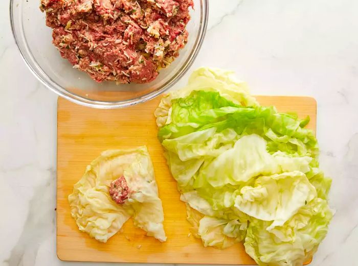 A close-up of cabbage leaves being filled with a hearty mixture on a cutting board