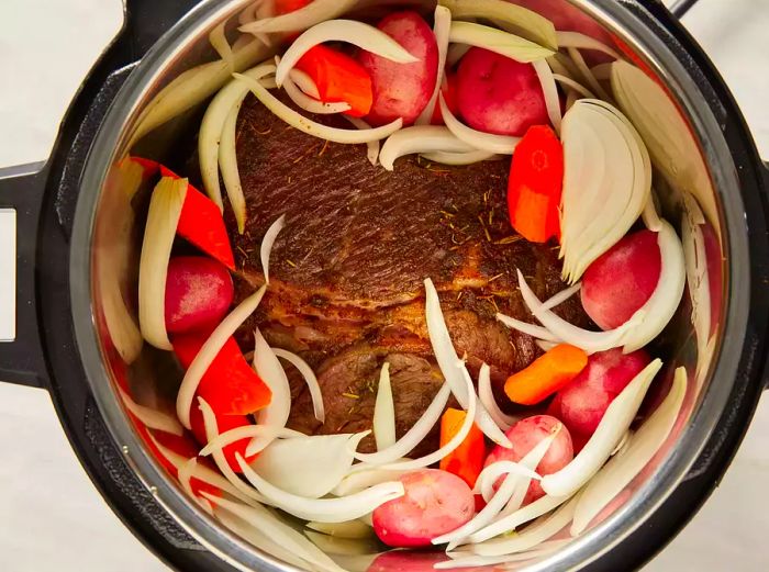 Chopped vegetables placed atop a roast cooking inside a pressure cooker.