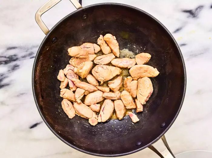 A wok containing browned slices of pork tenderloin cooked in sesame oil