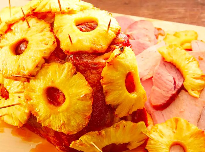 A brown sugar and pineapple glazed ham resting on a cutting board, with a few slices already cut.