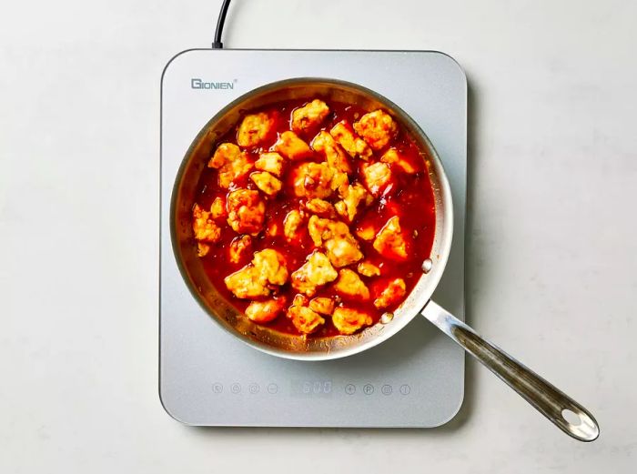 Crispy fried chicken being tossed in a saucepan with the savory General Tso's sauce.