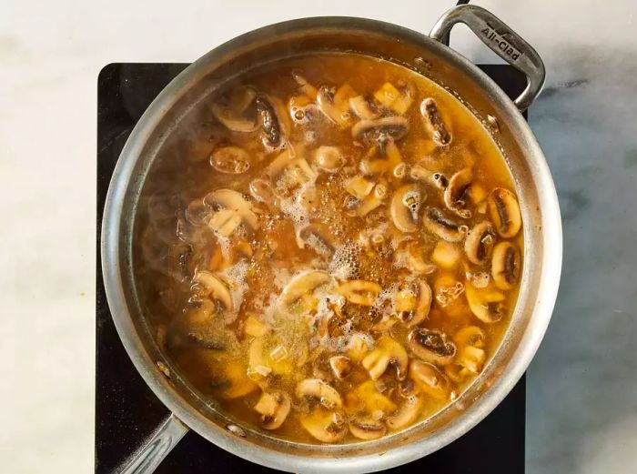 A skillet with sautéed mushrooms and shallots simmering in white wine