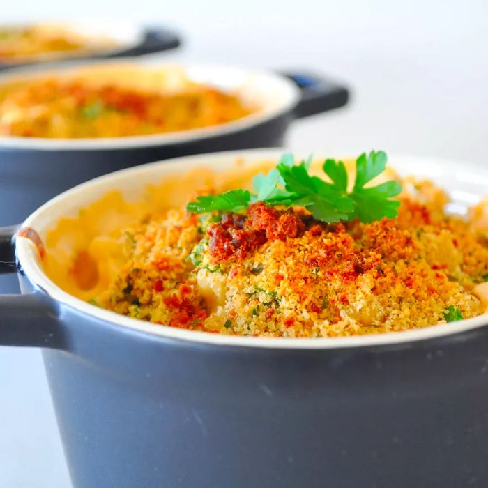 A close-up view of Macaroni and Cheese garnished with fresh herbs, served in grey ramekins.