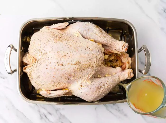 A person adding turkey stock into a roasting pan.