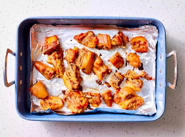 A roasting pan lined with foil and containing roasted pig tails