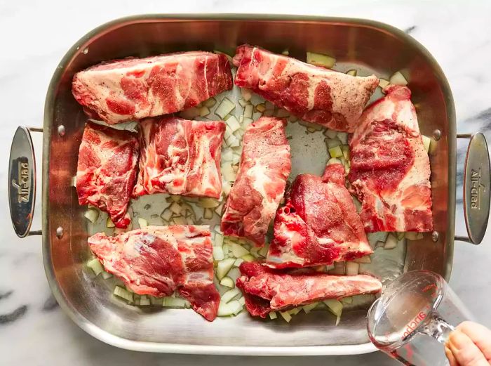 Aerial view showing neck bones in a roasting pan with garlic, onions, and a mixture of water and vinegar.