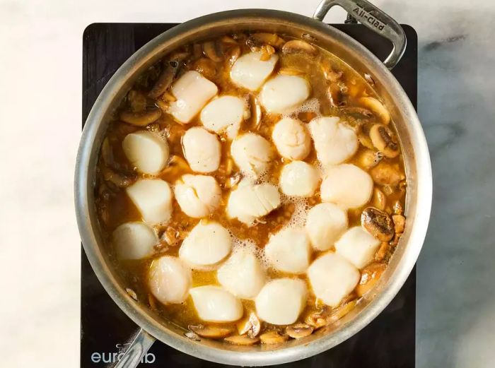 A pan with sautéed mushrooms, shallots, and scallops simmering in white wine