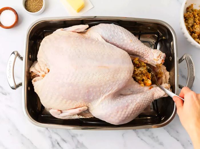 A person stuffing the cavity of a turkey with filling.