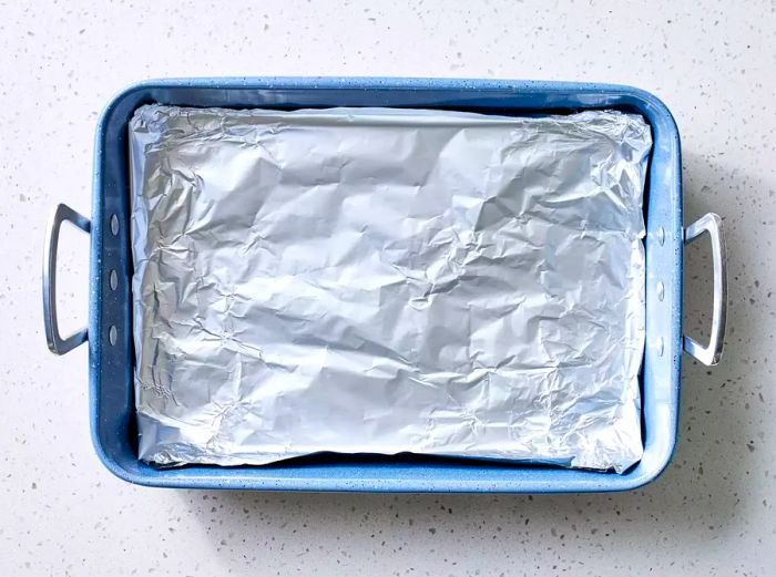 A roasting pan that has been lined with aluminum foil