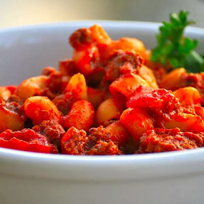 Close-up shot of goulash garnished with fresh herbs in a white bowl.