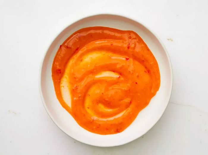 A large, shallow bowl filled with a creamy blend of mayonnaise, honey, sweet chili sauce, and gochujang, perfectly mixed together.