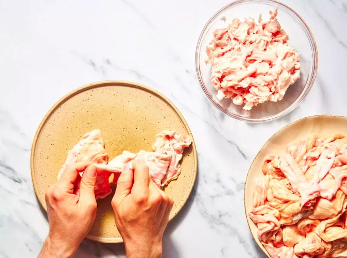 Two hands carefully cleaning chitterlings, with a bowl of thoroughly cleaned chitterlings beside them.