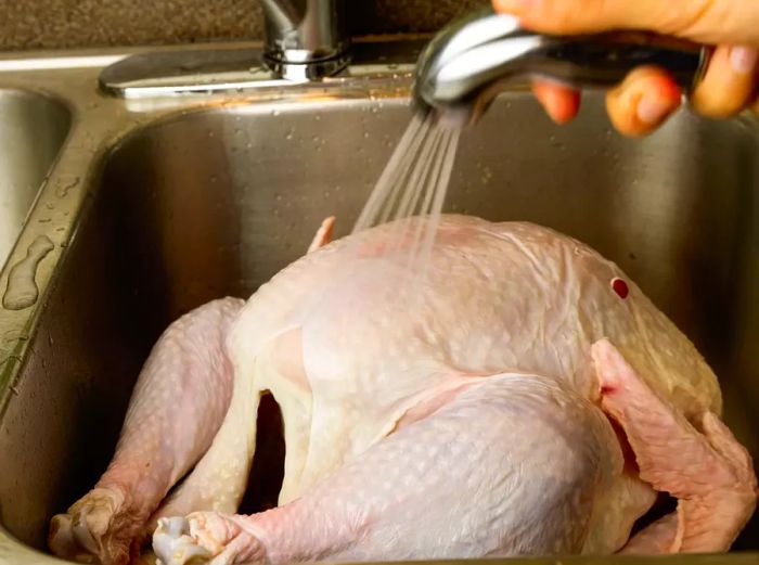 A raw turkey being rinsed under cold water in the sink.