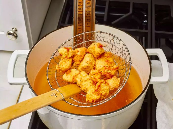 A mesh spider lifting golden fried chicken pieces from the hot oil.