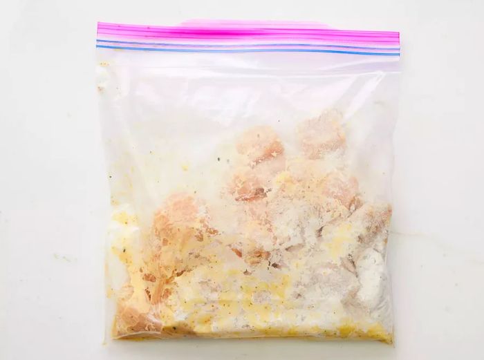 A large ziplock bag filled with cubed chicken breasts, fully coated in the flour mixture.