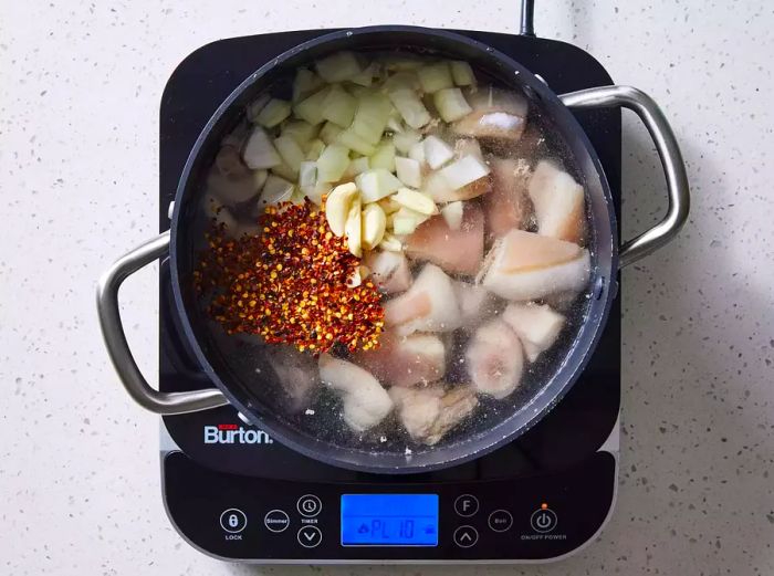 A large pot containing pig tails, water, garlic, onions, pepper flakes, and salt