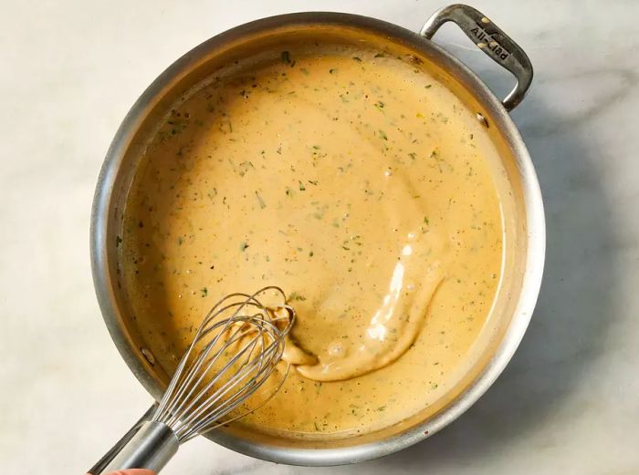 A pan of rich cream sauce being whisked to thicken