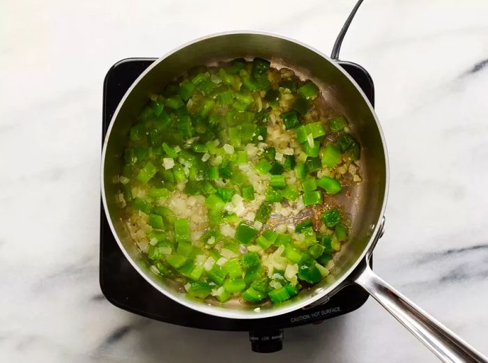 A top-down view of diced onion and green pepper cooking in a pot.