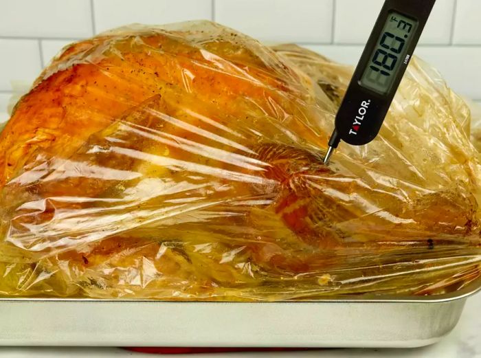 A cooking thermometer inserted into the turkey thigh while the bird sits in the bag within a baking dish.