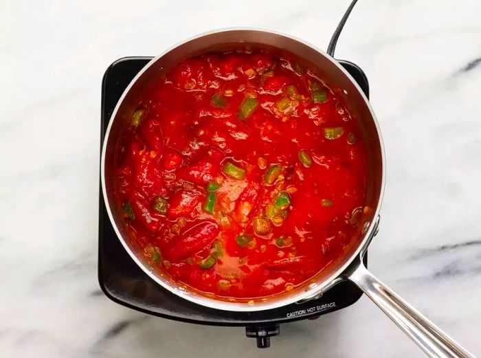 An overhead shot of a pot simmering with a tomato, onion, and green pepper sauce.