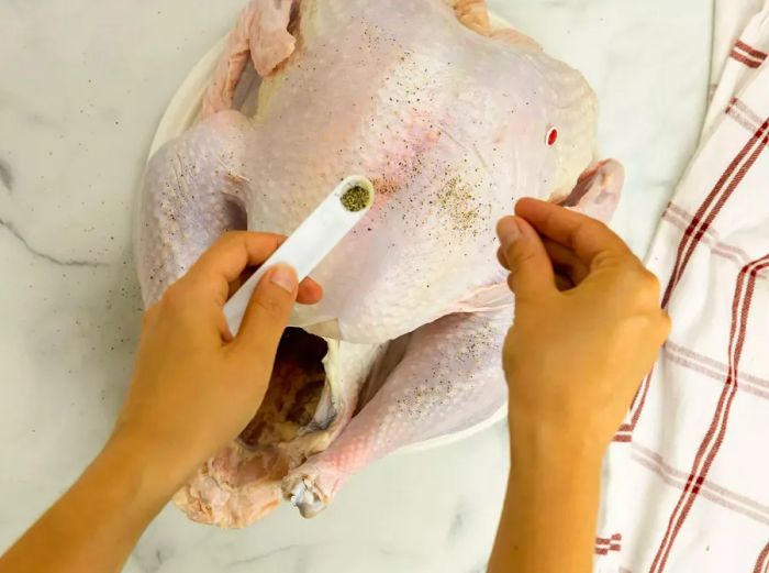 A raw turkey being seasoned with a pinch of salt and a dash of pepper.