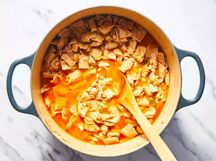 A large pot of cooked Creole chitterlings being stirred with a wooden spoon.