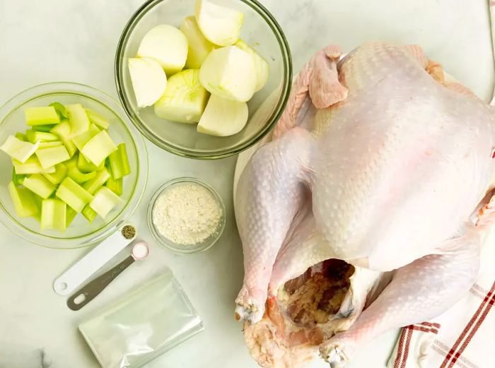 A raw turkey, celery, onions, and seasonings neatly arranged on a countertop.