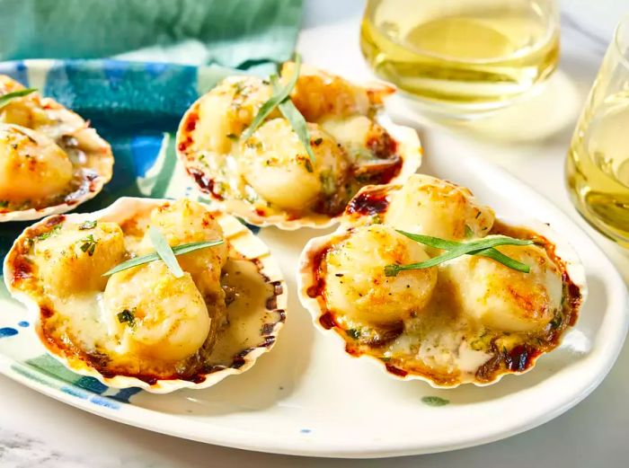 A plate of Coquilles Saint-Jacques served in their shells, beautifully garnished with tarragon leaves