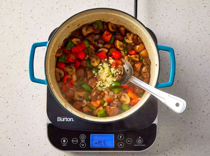 Minced garlic is added to the cooking vegetables.