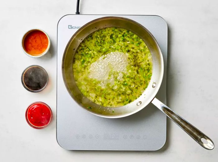 Sautéing green onions and ginger in a saucepan with sauces to create the base for General Tso's chicken.