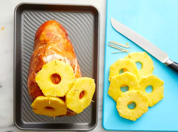 Pineapple rings being attached to the ham with toothpicks.