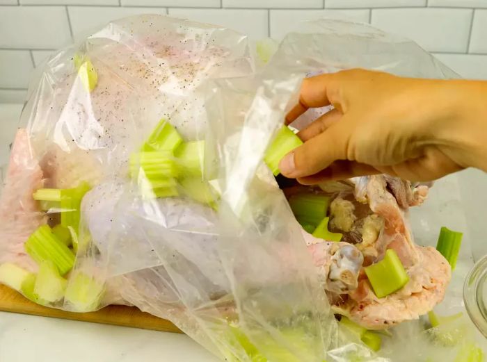 A turkey in a bag with someone adding celery and onions.