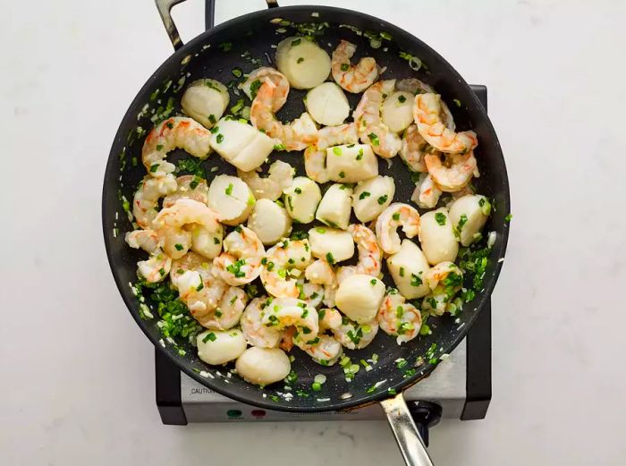 The green onions, shrimp, and scallops cooked together in the skillet with butter.