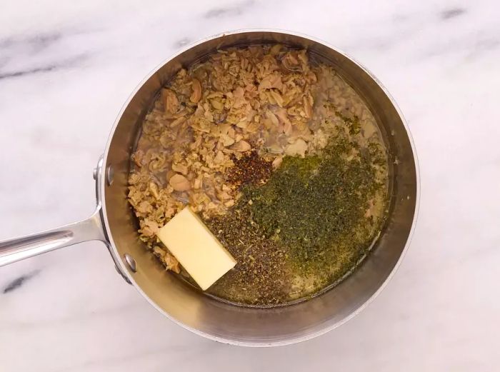 A skillet with clams in juice, oil, butter, parsley, basil, garlic, and pepper