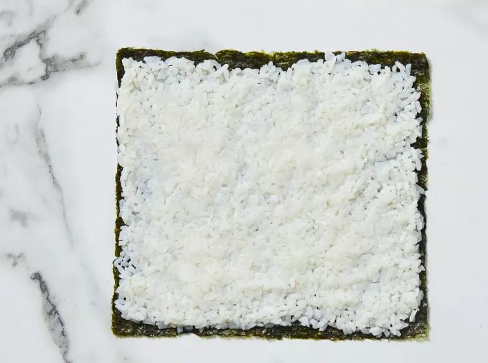 A layer of rice is spread over the nori sheet.