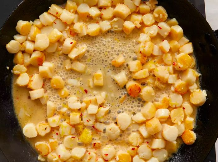 Aerial view of scallops, lemon zest, red pepper flakes, and sherry cooking together in a skillet.