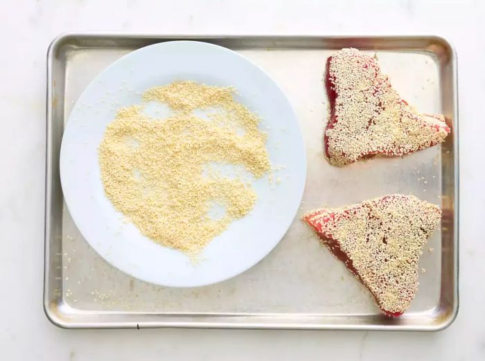 A plate filled with sesame seeds and two tuna steaks covered in the seeds.