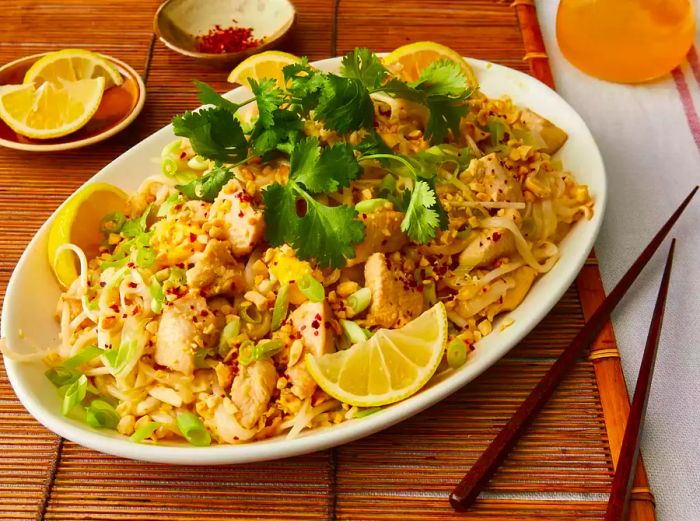 A view of a large platter of pad Thai, beautifully garnished with fresh herbs and lemon wedges.