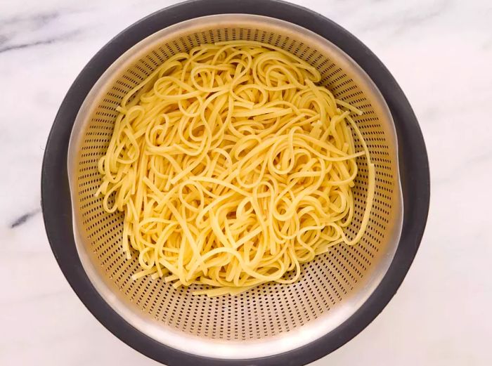 A metal strainer holding the cooked linguine pasta