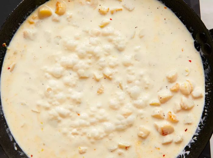 Aerial view of bubbling cream and scallop mixture simmering in a skillet.