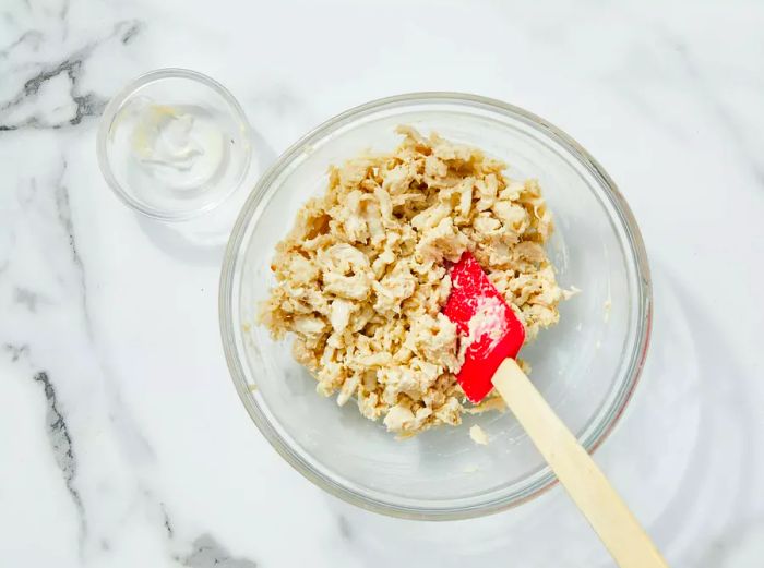 Crab meat and mayo are stirred together in a bowl.