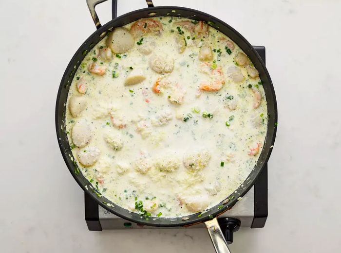 Half-and-half, seasonings, and Parmesan cheese have been added to the skillet.