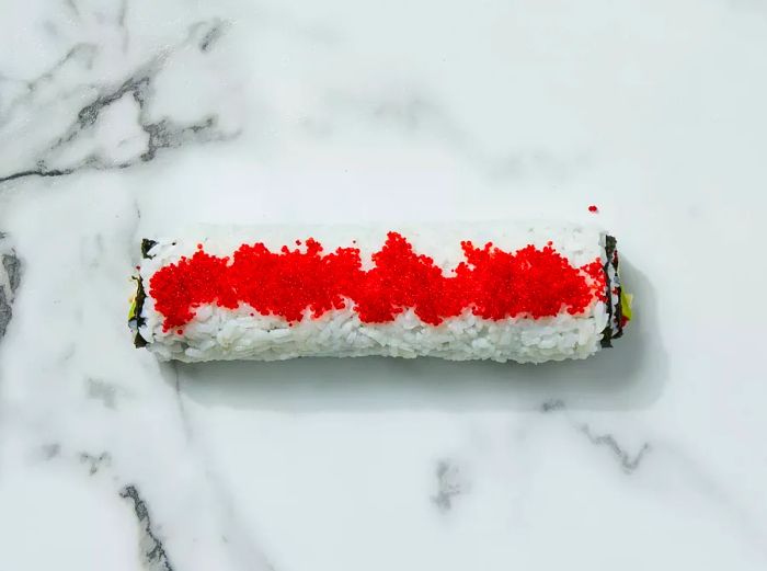 Roll the sushi tightly and sprinkle additional tobiko on top.