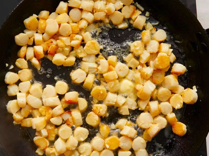 Aerial view of scallops cooking with butter and garlic in a skillet.