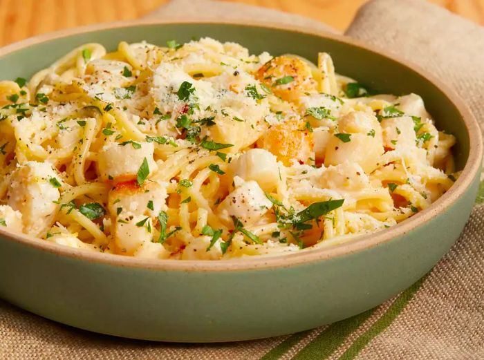 A mid-angle view of a bowl filled with creamy bay scallop spaghetti, garnished with fresh herbs.