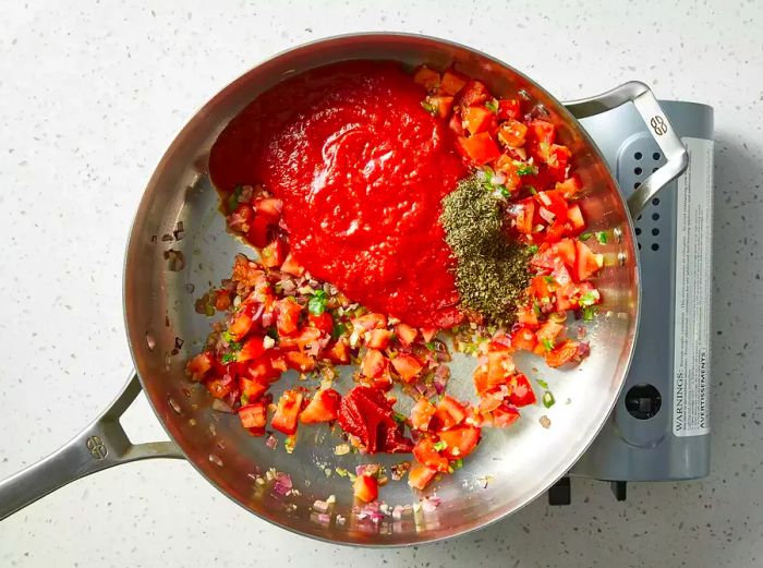 A bird's-eye view of tomato paste, oregano, and thyme being added to the pan