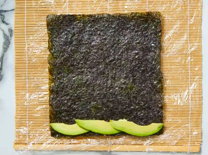 Flip the nori and rice so the rice is facing down, then add a few slices of avocado on top of the nori.