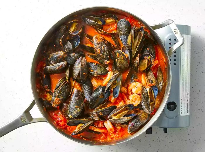 A top-down view of seafood marinara pasta sizzling in a pan